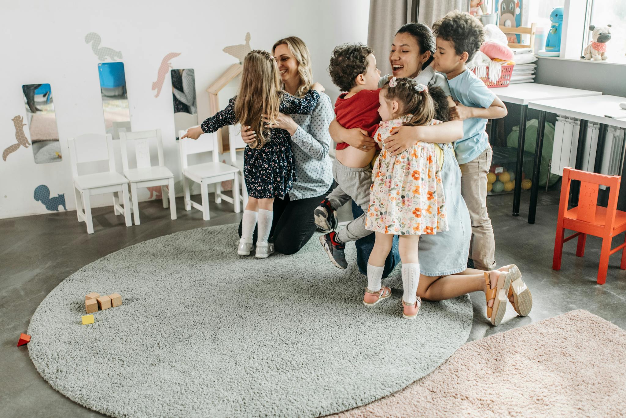 A group of children happily hugging their teachers in a kindergarten classroom.