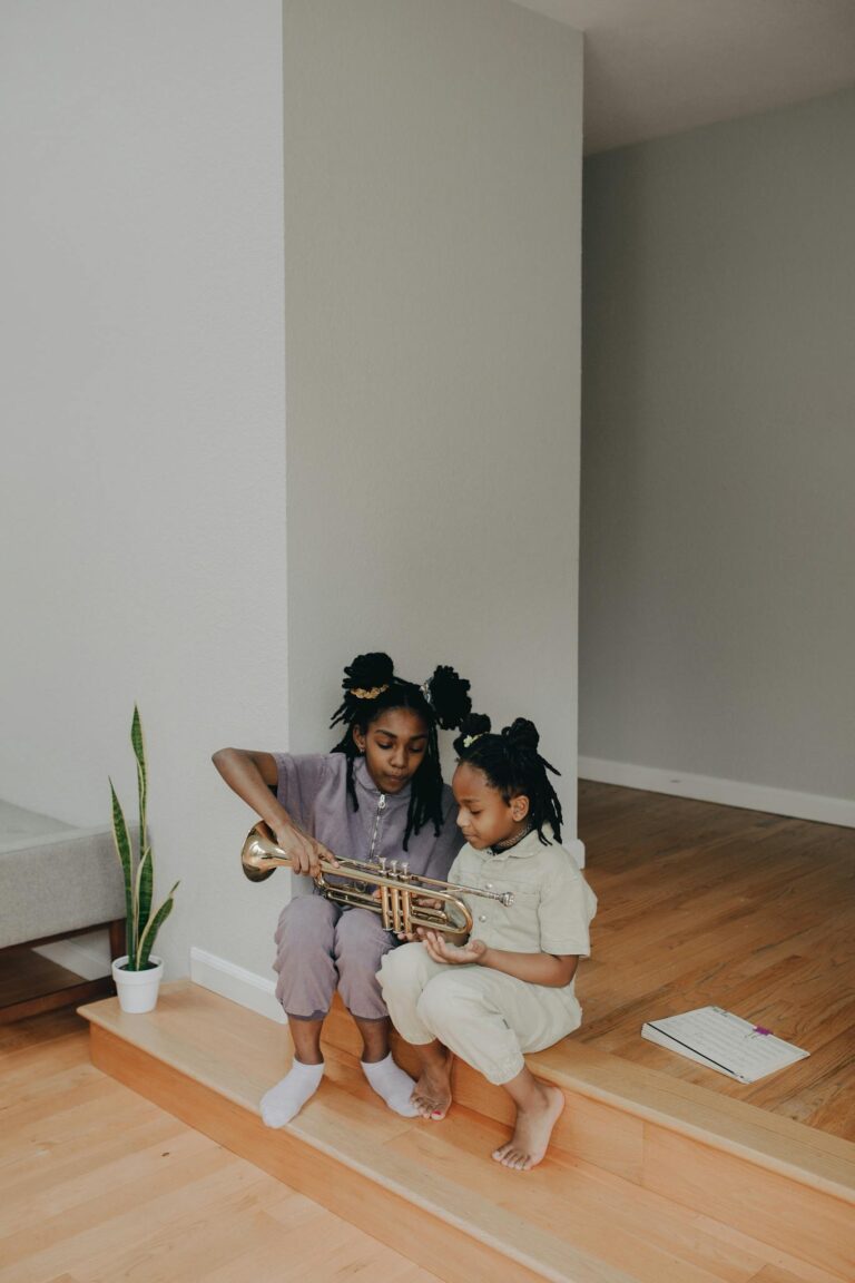 Two sisters sitting indoors, learning to play a trumpet together, fostering musical growth.