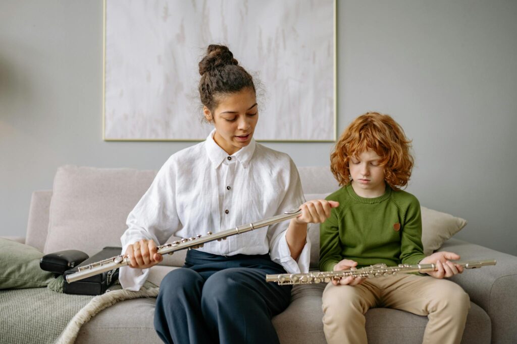 Woman and child engaged in a music lesson with flutes on a sofa indoors.